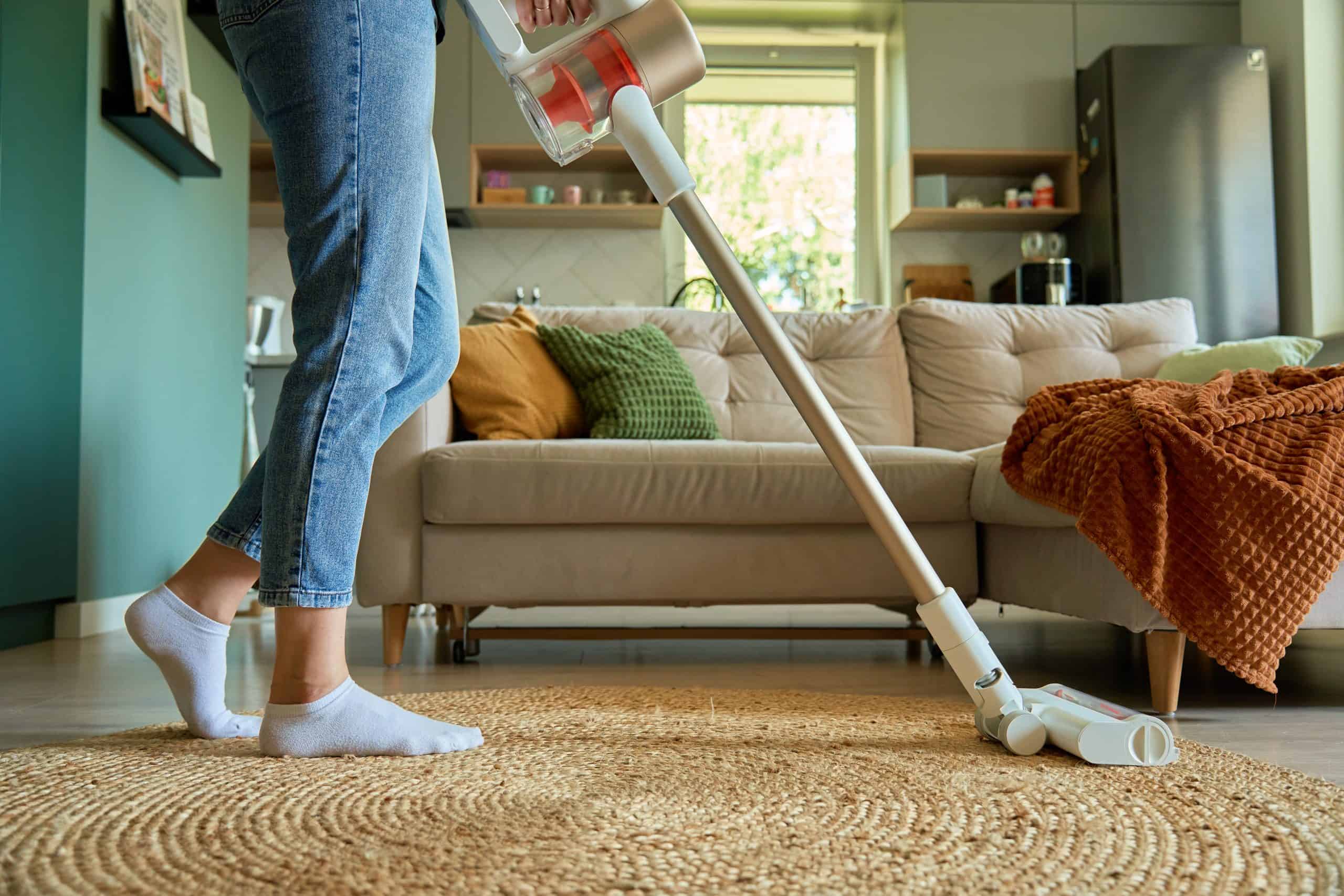 Person saugt Wohnzimmerboden mit modernem Staubsauger, Fokus auf Beinen und Gerät.
